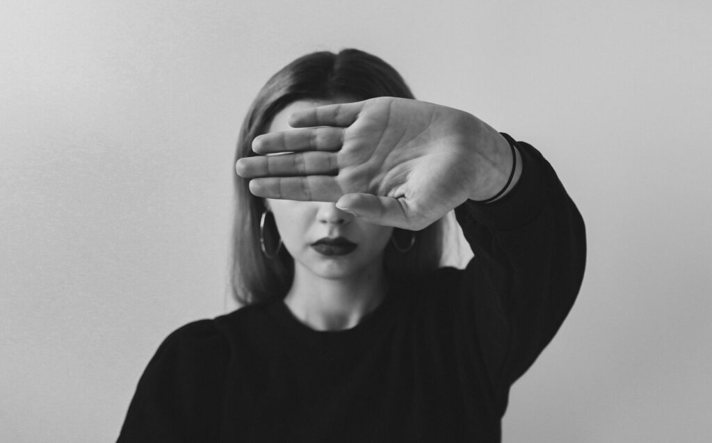 Frau verdeckt ihr Gesicht mit der Hand. Symbolbild für den inneren Kritiker und Selbstzweifel